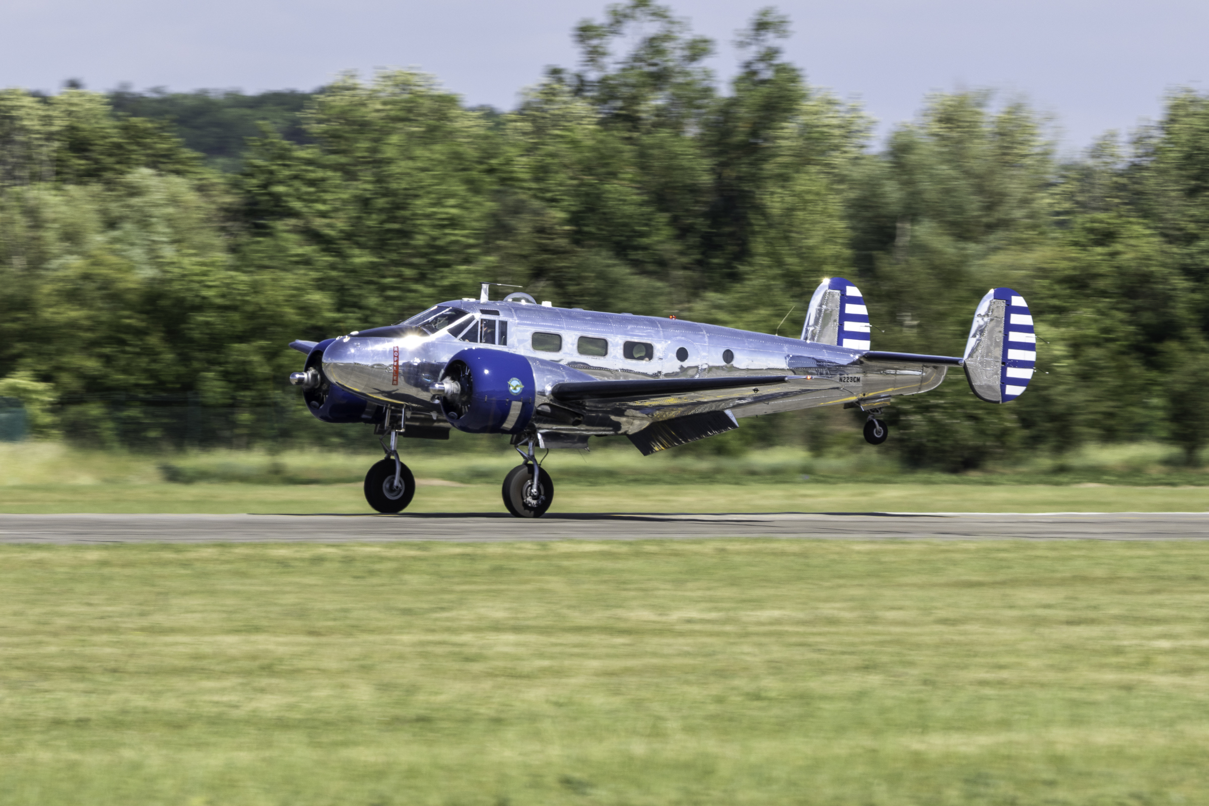 Polished-metal Beechcraft Model 18 with blue engine cowlings lifting off the runway