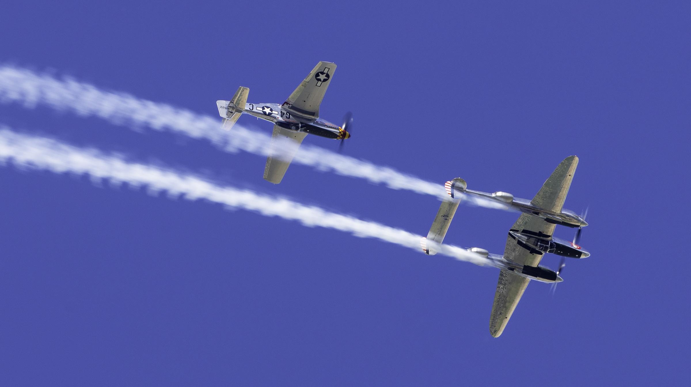 P-51 Mustang and P-38 Lightning in a formation pass with white smoke trails